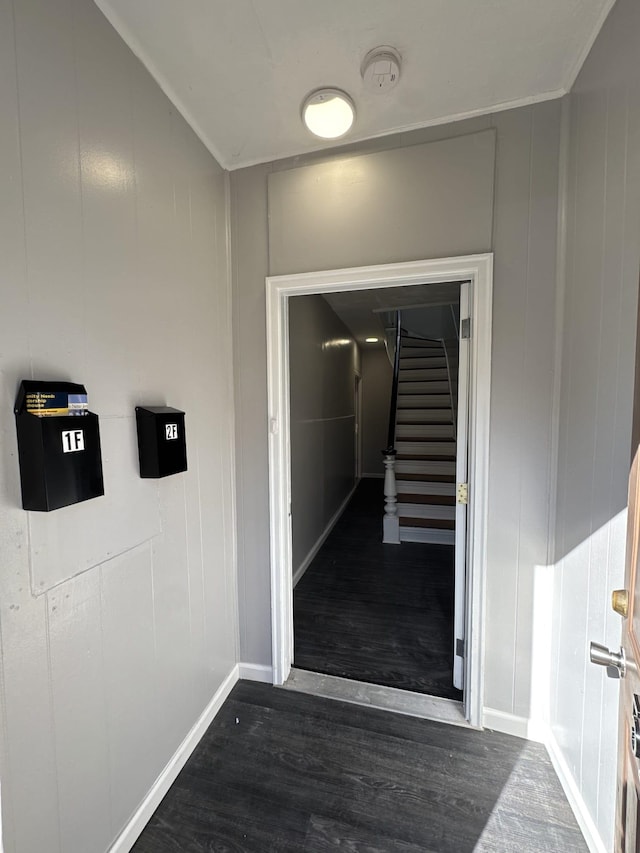 corridor with dark wood-type flooring, baseboards, stairway, and a decorative wall