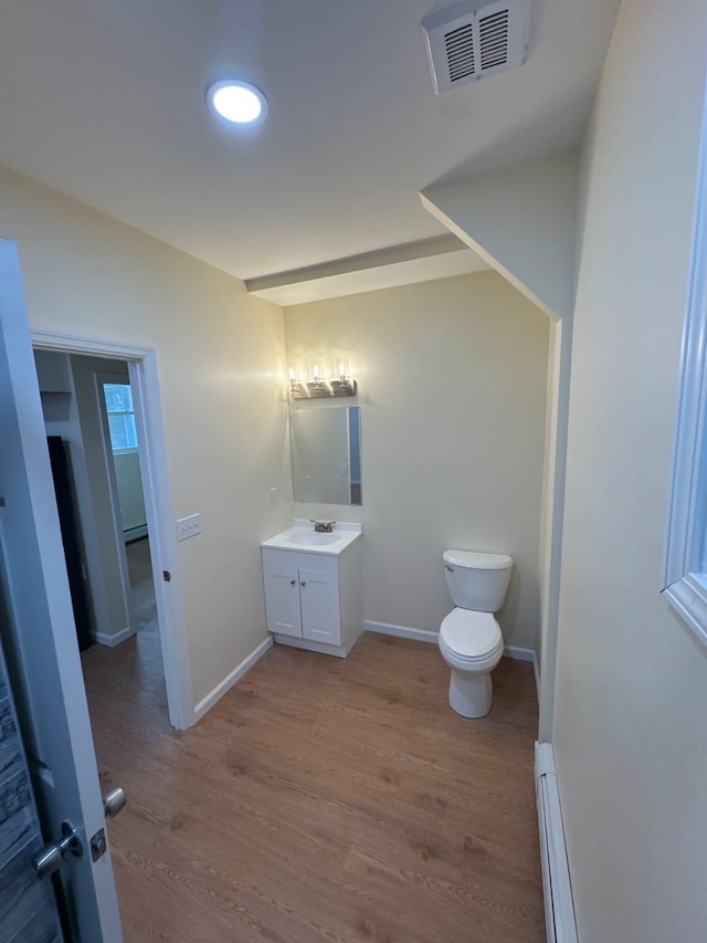 half bathroom with vanity, baseboard heating, toilet, visible vents, and wood finished floors