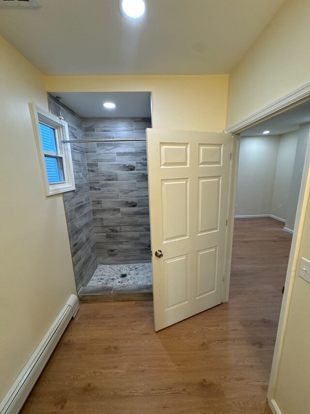 bathroom featuring a tile shower, recessed lighting, wood finished floors, a baseboard radiator, and baseboards