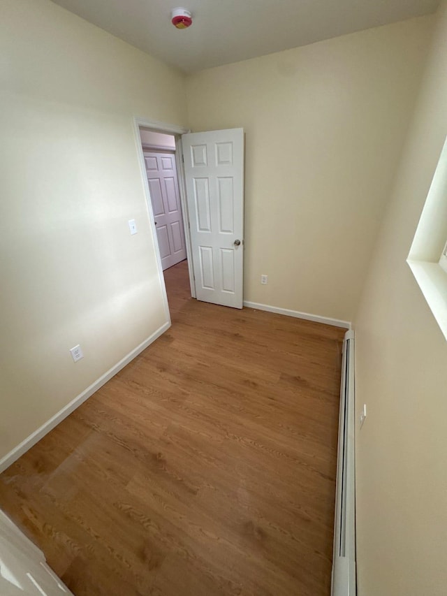 spare room with baseboards, a baseboard heating unit, and wood finished floors