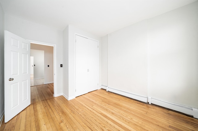 unfurnished room with baseboard heating, baseboards, and light wood-style flooring