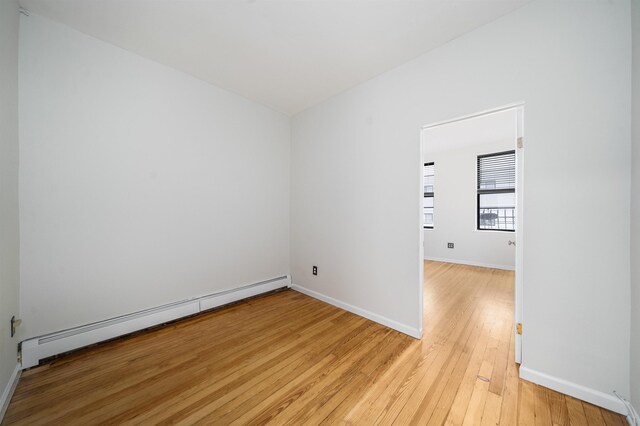 empty room featuring baseboards, a baseboard heating unit, and light wood-style flooring