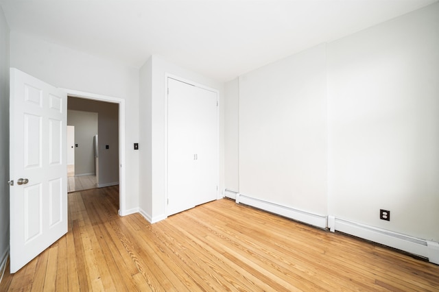 unfurnished bedroom featuring baseboards, a baseboard radiator, light wood finished floors, and a closet