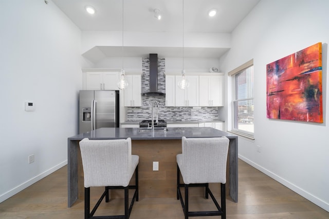 kitchen with wood finished floors, stainless steel fridge with ice dispenser, decorative backsplash, a kitchen bar, and wall chimney exhaust hood