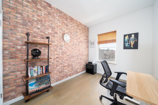 office space with wood finished floors, baseboards, and brick wall