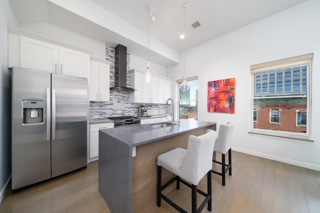 kitchen with visible vents, a sink, stainless steel appliances, wall chimney range hood, and backsplash