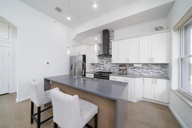 kitchen featuring gas stove, visible vents, a sink, wall chimney exhaust hood, and stainless steel fridge