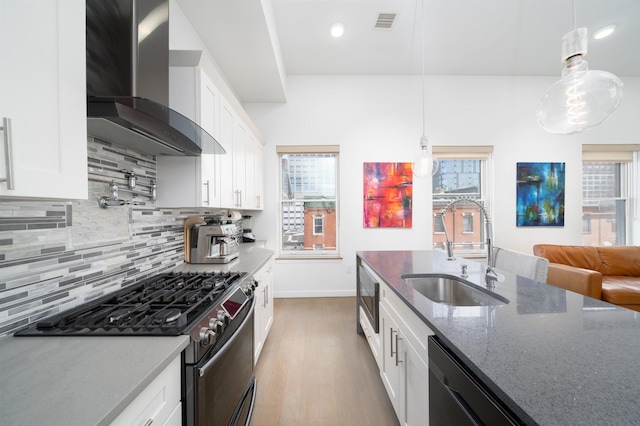 kitchen featuring dark stone countertops, stainless steel appliances, white cabinetry, wall chimney exhaust hood, and a sink