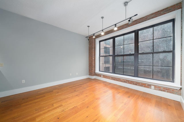 spare room with brick wall, a wealth of natural light, and hardwood / wood-style floors