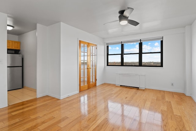 empty room featuring a healthy amount of sunlight, radiator, light hardwood / wood-style flooring, and french doors