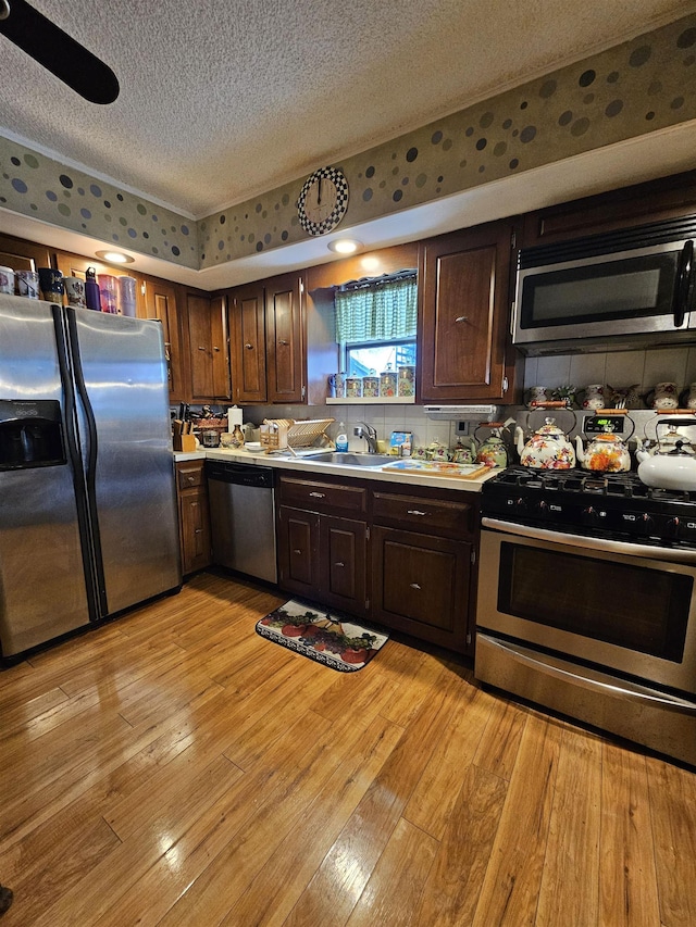 kitchen with sink, a textured ceiling, dark brown cabinets, light hardwood / wood-style floors, and stainless steel appliances