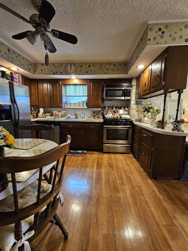 kitchen with appliances with stainless steel finishes, light wood-type flooring, a textured ceiling, dark brown cabinetry, and ceiling fan