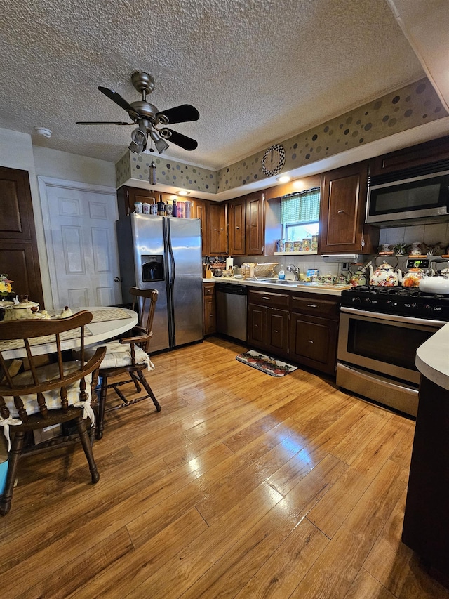 kitchen featuring light wood-type flooring, a textured ceiling, stainless steel appliances, ceiling fan, and sink