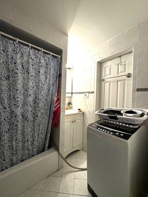 bathroom featuring vanity, tile patterned flooring, tile walls, shower / tub combo with curtain, and washer / dryer