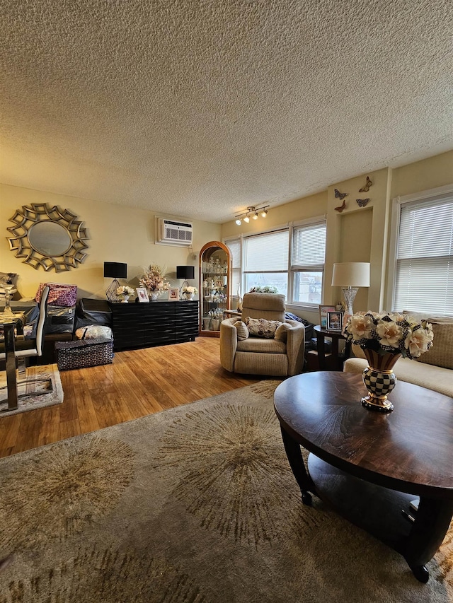 living room with a wall mounted air conditioner, wood-type flooring, a textured ceiling, and track lighting