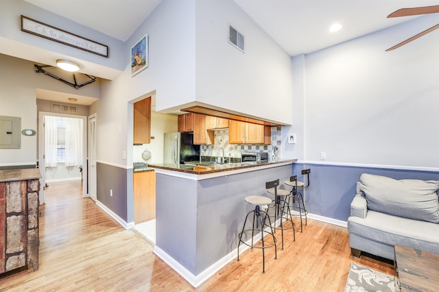 kitchen featuring light wood finished floors, a breakfast bar area, visible vents, freestanding refrigerator, and a peninsula