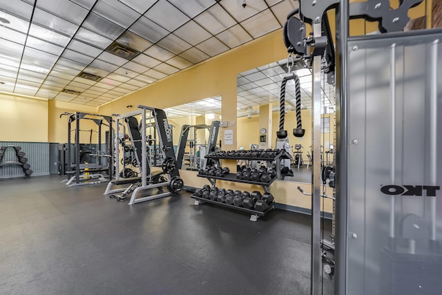 workout area with a wainscoted wall, visible vents, and a drop ceiling