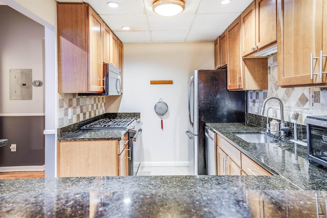 kitchen featuring a paneled ceiling, appliances with stainless steel finishes, a sink, dark stone counters, and electric panel