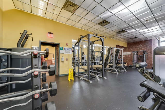 exercise room featuring a paneled ceiling, brick wall, and visible vents