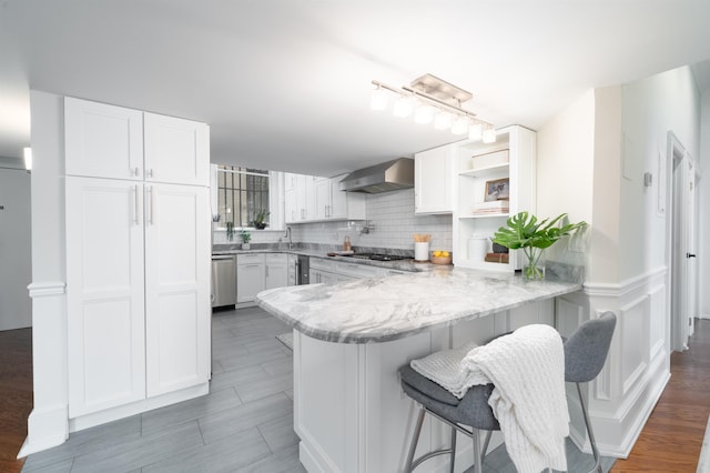 83 Montgomery St Unit 201, Jersey City, NJ 07302 - kitchen featuring wall chimney range hood, a peninsula, white cabinets, tasteful backsplash, and a kitchen breakfast bar