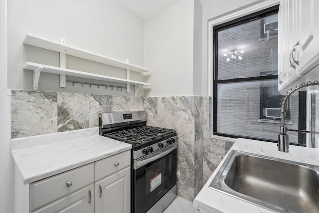 kitchen with stainless steel gas stove, light stone counters, white cabinetry, and sink