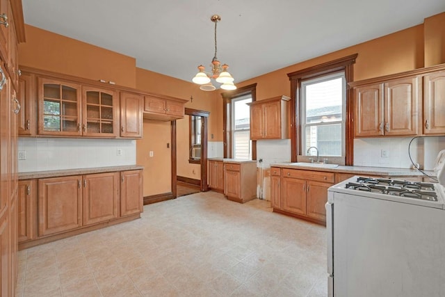 kitchen featuring a sink, glass insert cabinets, white gas range oven, decorative backsplash, and hanging light fixtures