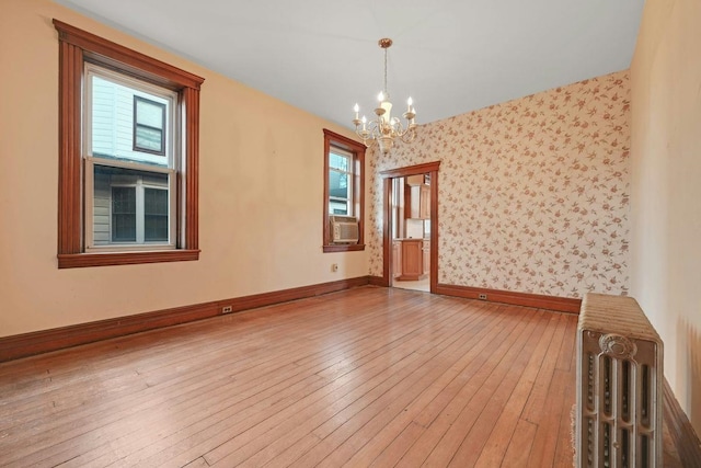 unfurnished room with wallpapered walls, baseboards, an inviting chandelier, and hardwood / wood-style floors