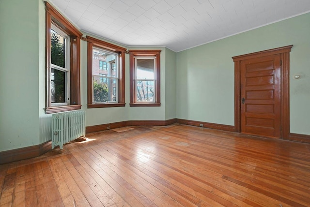 empty room with radiator, baseboards, light wood finished floors, and ornamental molding