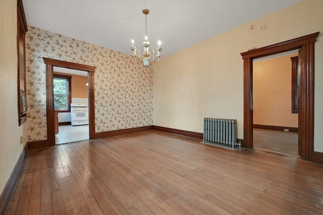 empty room featuring a chandelier, radiator, wallpapered walls, and hardwood / wood-style flooring