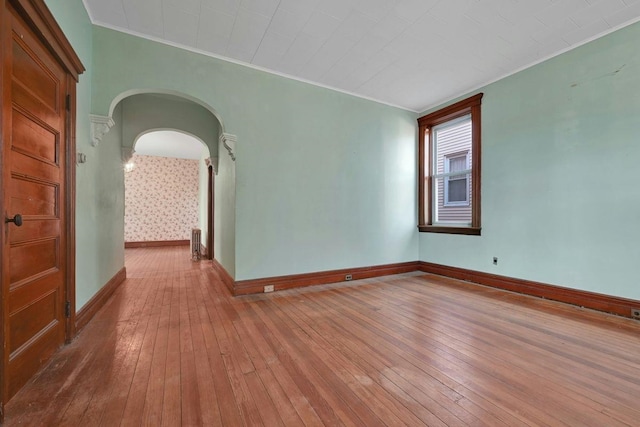 unfurnished room with arched walkways, ornamental molding, baseboards, and hardwood / wood-style flooring