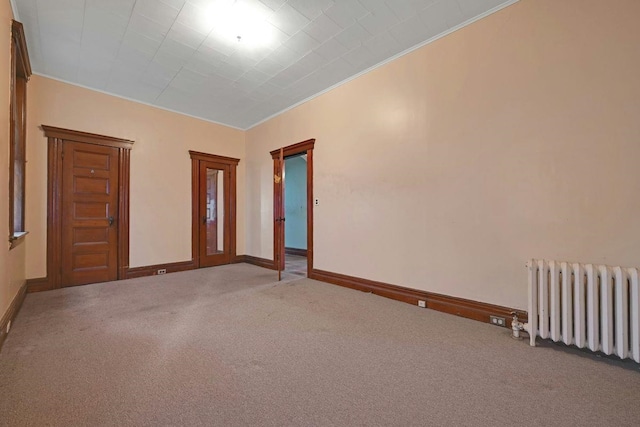 unfurnished room with baseboards, radiator, crown molding, and carpet