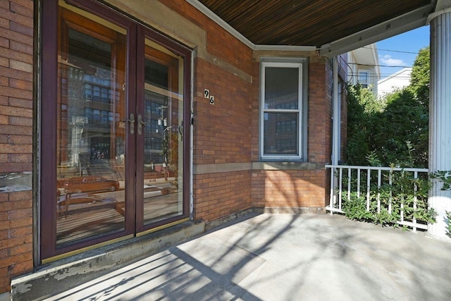 view of exterior entry with french doors, brick siding, and covered porch