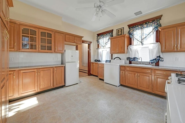 kitchen with brown cabinetry, freestanding refrigerator, a sink, stove, and glass insert cabinets