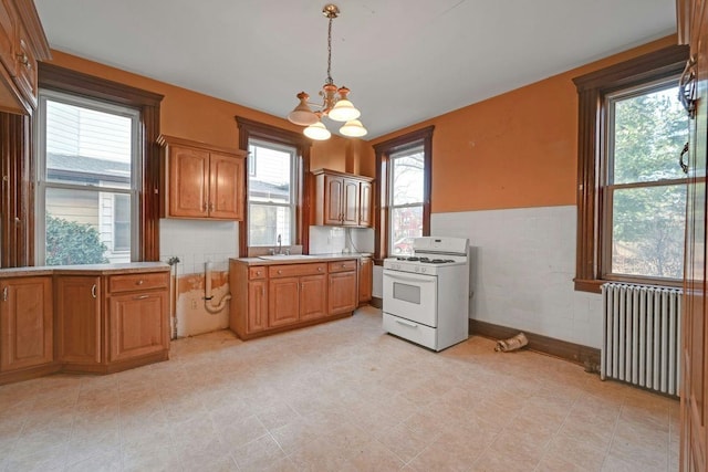 kitchen with a sink, radiator, wainscoting, light countertops, and white range with gas stovetop