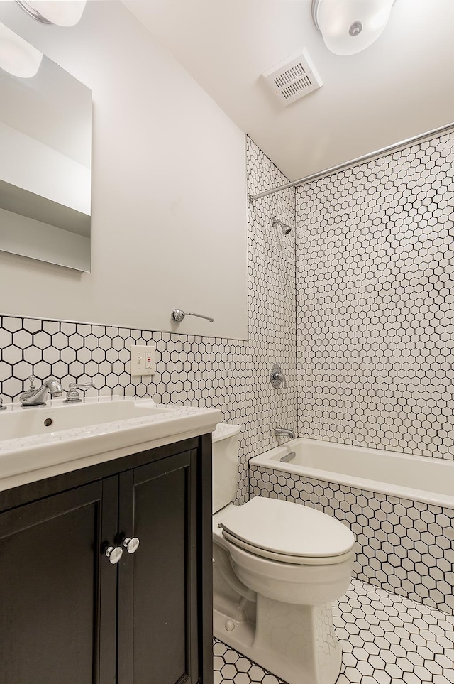 full bathroom with vanity, tiled shower / bath, tile patterned flooring, toilet, and tile walls