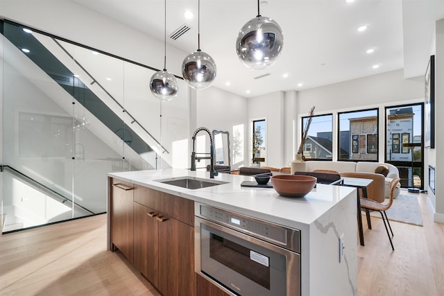 kitchen featuring pendant lighting, sink, light wood-type flooring, and an island with sink