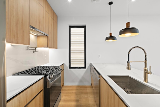 kitchen featuring modern cabinets, appliances with stainless steel finishes, decorative light fixtures, light wood-style floors, and a sink