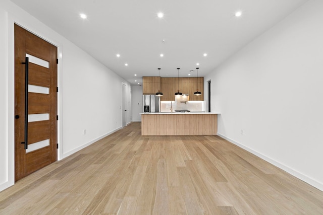 kitchen with light wood-style flooring, open floor plan, a peninsula, light countertops, and pendant lighting