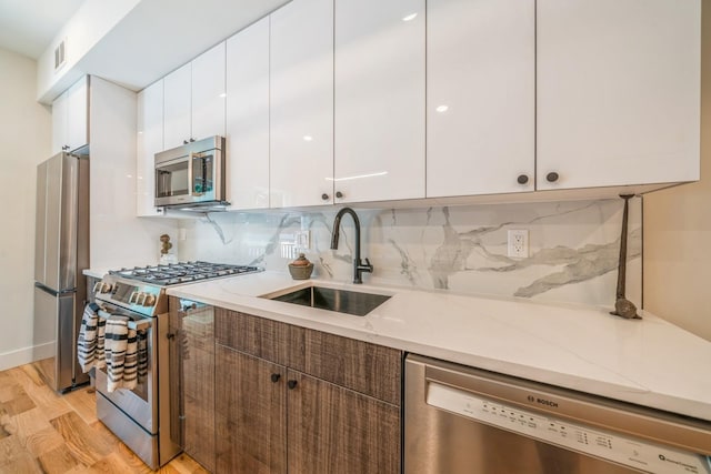 kitchen with sink, light hardwood / wood-style flooring, appliances with stainless steel finishes, white cabinets, and decorative backsplash