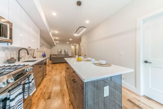 kitchen with sink, hanging light fixtures, a kitchen island, stainless steel appliances, and white cabinets