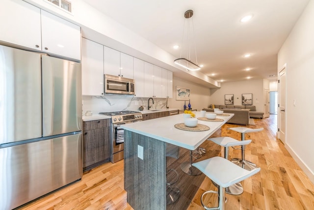 kitchen with pendant lighting, tasteful backsplash, white cabinets, stainless steel appliances, and light hardwood / wood-style flooring