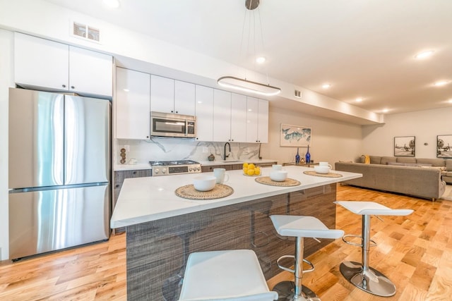 kitchen with stainless steel appliances, a center island, light hardwood / wood-style floors, white cabinets, and decorative light fixtures