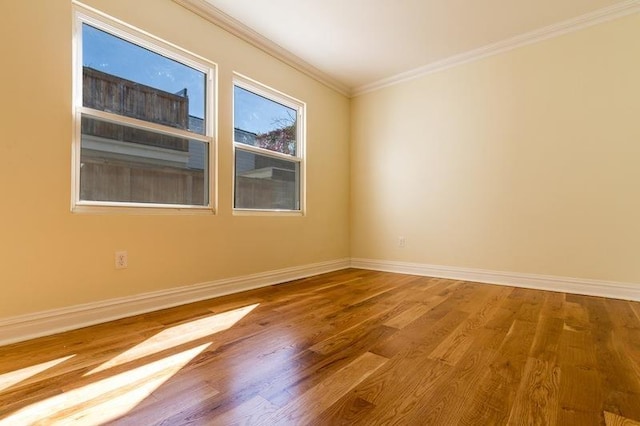 empty room featuring crown molding, baseboards, and wood finished floors