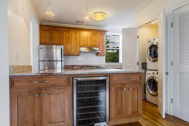 kitchen with brown cabinetry, wine cooler, freestanding refrigerator, under cabinet range hood, and stacked washing maching and dryer