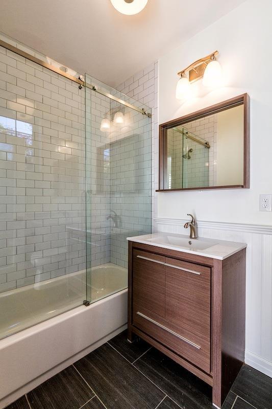 full bath with combined bath / shower with glass door, wainscoting, wood finished floors, and vanity