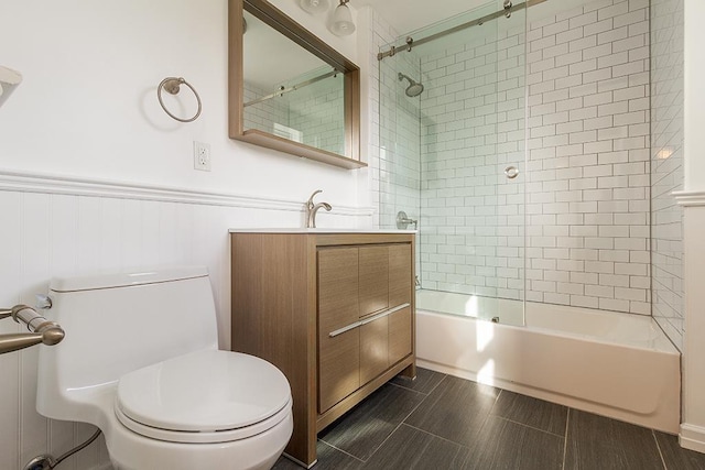 bathroom with toilet, a wainscoted wall, shower / bath combination with glass door, and vanity