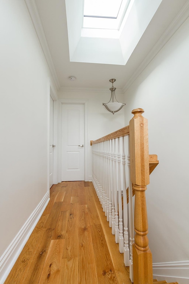 corridor featuring ornamental molding, a skylight, light wood-style flooring, and baseboards