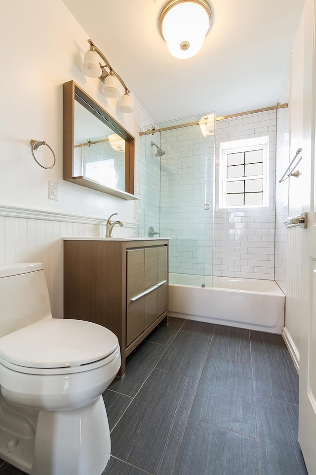 full bath with wainscoting, vanity, toilet, and bath / shower combo with glass door