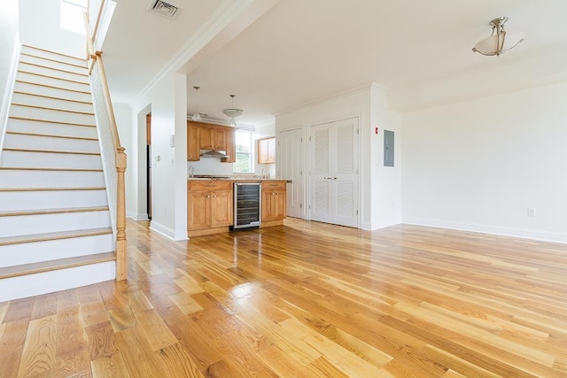 unfurnished living room with wine cooler, visible vents, stairway, light wood-style floors, and ornamental molding