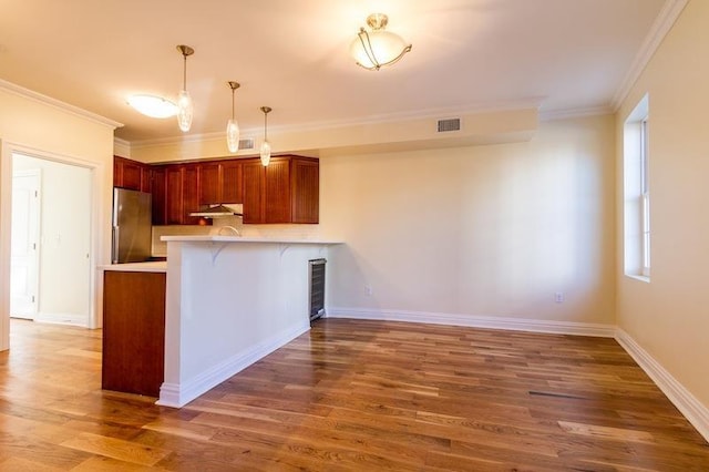 kitchen featuring a breakfast bar, light countertops, freestanding refrigerator, a peninsula, and under cabinet range hood